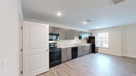 This thoughtfully designed single-story unit in Selmer, Tennessee, offers a clean, modern aesthetic throughout its efficiently organized floor plan. Light-toned luxury vinyl plank flooring runs continuously across all living areas, lending the space a cohesive and contemporary feel.

The open-concept kitchen and living area serves as the heart of the unit. The kitchen is outfitted with dark gray cabinetry extending to the ceiling for generous storage, light stone-look countertops, and a full suite of black appliances including a range, over-the-range microwave, dishwasher, and refrigerator. A window above the counter allows natural light to brighten the workspace.

The living room is a generously sized, bright area with neutral walls and a set of double glass doors that open to an outdoor view of lush greenery, filling the space with natural light and a sense of openness. A hallway connects the living areas to the private quarters, maintaining a practical flow throughout.

The spacious primary bedroom features a ceiling fan, a well-sized window with outdoor views, and ample room for furnishings. The full bathroom includes dark cabinetry with a tall storage tower, a light stone countertop vanity, and consistent vinyl flooring. A dedicated laundry room houses a full-size washer and dryer with overhead wire shelving for additional storage.