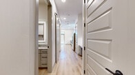 This single-floor, one-bedroom unit offers a thoughtfully designed layout with modern finishes throughout. Light wood-tone flooring runs continuously across all rooms, creating a cohesive and clean aesthetic. Recessed lighting illuminates the space, complemented by a ceiling fan in the living area, which also features double doors with a transom window above, allowing natural light to filter in.

The kitchen is well-appointed with gray flat-front cabinetry extending to the ceiling, granite countertops, a textured tile backsplash, and stainless steel appliances including a refrigerator with ice and water dispenser, electric range, and built-in microwave. A barn-style sliding door serves as a functional design detail in the hallway.

The bathroom features a granite-topped vanity with gray cabinetry, matte black hardware, a backlit mirror, and a tub-shower combination with large-format gray tile surround. The bedroom is compact yet functional, with access to a walk-in closet equipped with built-in shelving units and dual hanging rods on either side, maximizing storage efficiency. White walls throughout maintain a bright, neutral palette.