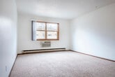 Located at 3335 East Ave S in La Crosse, Wisconsin, this 2-bedroom, 1-bathroom unit offers a practical and well-organized single-floor layout. The kitchen serves as a central hub, featuring warm wood-toned cabinetry that extends from floor to ceiling, a peninsula with a double-basin sink and light countertops, and a white electric range. Tile flooring flows through the kitchen and entry area, creating a clean transition into the carpeted living spaces. The primary bedroom is generously sized, offering soft carpeting, a ceiling fan with light fixture, a window with outdoor views, and baseboard heating. The second bedroom mirrors a similar aesthetic with plush carpeting, white walls, and a window that brings in natural light. Both bedrooms are finished with warm wood trim throughout. A dedicated closet provides built-in shelving and hanging space with bifold wood-paneled doors. The bathroom is clean and functional, featuring a full tub-shower combo with grab bars, a toilet, and a vanity with a granite-patterned countertop and mirrored cabinet above. Textured ceilings are consistent throughout the unit, contributing to its classic residential character.