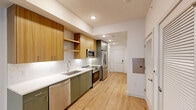 Located at 222 N West St in downtown Raleigh, NC, this thoughtfully designed one-bedroom, one-bathroom unit offers a modern and efficient layout across a single floor. Light-toned hardwood flooring flows throughout, creating a cohesive and welcoming ambiance.

The galley-style kitchen is a standout feature, showcasing sage green lower cabinets paired with warm wood-toned upper cabinetry and open shelving. A herringbone tile backsplash, white quartz countertops, and a full suite of stainless steel appliances — including a French door refrigerator, electric range, over-the-range microwave, and dishwasher — complete this well-appointed space.

The living area benefits from recessed lighting and an open feel that leads naturally to the bedroom. The bedroom is bright and comfortable, featuring a large window with outdoor views of the surrounding Raleigh streetscape and a ceiling fan for added comfort. Three closets throughout the unit provide generous storage options.

The bathroom offers a clean, modern aesthetic with white subway tile surrounding a full soaking tub and shower combination, complemented by chrome fixtures, a vanity with a white countertop, and hardwood-style flooring. A dedicated utility room and electrical panel access round out the practical amenities of this well-planned unit.