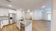 Located at 6801 Burnet Rd in Austin, TX, this thoughtfully designed 2-bedroom, 2-bathroom residence offers a clean, modern aesthetic across a single floor. The open-concept kitchen and living area serves as the heart of the home, anchored by a central island with a quartz countertop, undermount sink, and matte black faucet. White shaker cabinetry, a subway tile backsplash, and stainless steel appliances — including a side-by-side refrigerator, range, microwave, and dishwasher — complete the kitchen. Pendant lighting above the island and recessed ceiling lights add layered illumination throughout. Light wood-tone flooring runs seamlessly through the main living areas, creating a warm, cohesive feel, while plush carpet adds comfort to the bedrooms. The primary bedroom features a ceiling fan and dedicated closet. Both bathrooms are finished with white cabinetry and matte black hardware; the primary bath includes a dual-sink vanity with a large framed mirror, while the secondary bath offers a tiled tub-shower combination. Each bedroom is bright and airy, with natural light from window treatments. The space also includes two closets for ample storage, making it a well-appointed and functional Austin residence.
