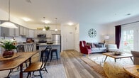 This single-floor residence offers a thoughtfully designed open-concept layout that seamlessly connects the kitchen, dining, and living areas. The kitchen is a functional highlight, featuring gray cabinetry, granite countertops, stainless steel appliances, and a center island with bar seating illuminated by pendant lighting. Wood-look flooring flows throughout the main living areas, adding warmth and continuity to the space.

The dining area sits adjacent to the kitchen and provides a dedicated space for meals, accented by a pendant light and white paneled doors leading to other areas of the home. The living room is generously sized, anchored by French doors that invite natural light and provide views of the outdoors. The space is comfortable and welcoming, with neutral walls that complement a variety of décor styles.

The bedroom is bright and airy, benefiting from multiple windows dressed with blinds and curtains. It includes a walk-in closet for ample storage and direct access to a private full bathroom. The bathroom features a vanity with a white countertop, a dark cabinet base, and a shower, finished with clean, neutral tones throughout.