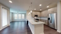 This 3-bedroom, 2-bathroom residence in Duluth, GA features a thoughtfully designed single-story layout with modern finishes throughout. The open-concept living and kitchen area serves as the heart of the home, where dark hardwood-style flooring flows seamlessly underfoot. The kitchen is equipped with light wood cabinetry, granite countertops, a subway tile backsplash, stainless steel appliances including a gas range, microwave, and French door refrigerator, and a peninsula island with pendant lighting overhead and an undermount sink. The living area offers ample natural light through multiple windows and includes a ceiling fan for added comfort. The bedrooms are carpeted and well-sized, each featuring ceiling fans with lighting and windows that bring in natural light. The primary bathroom is appointed with granite countertops, a wood-toned vanity, dark hardwood-style flooring, and access to a walk-in closet. The secondary bathroom mirrors this refined aesthetic with matching granite countertops, a wood-toned vanity, and a tiled tub-shower combination. Recessed lighting throughout enhances the clean, contemporary ambiance of this well-appointed Duluth residence.