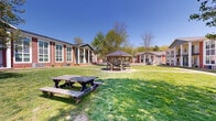 Located at 3512 Branchwood Dr in Evansville, Indiana, this single-story residential complex presents a classic and well-maintained aesthetic defined by its distinctive red brick exterior, white trim accents, and large multi-pane windows that allow abundant natural light throughout. The building's façade features a welcoming covered entryway supported by white columns, with an upper-level balcony that adds architectural dimension and provides elevated outdoor space for residents.

The grounds are a standout feature of this property, offering generously sized, well-kept green lawns that extend across the community. Mature trees are thoughtfully positioned throughout the landscape, providing natural shade and enhancing the overall sense of tranquility. A wooden gazebo with picnic table seating serves as a central gathering point, ideal for outdoor relaxation and socializing. An additional open-air pavilion, constructed with sturdy dark-stained timber framing and set on a concrete pad, offers a versatile covered outdoor space suitable for a variety of community activities.

Paved walkways connect the various outdoor areas, ensuring convenient access throughout the grounds. The surrounding neighborhood adds to the community feel, with additional residential buildings visible nearby. Overall, the property combines durable brick construction with thoughtfully designed communal outdoor amenities, creating a comfortable and functional living environment.