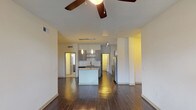 This single-floor residence offers a well-designed open-concept layout that seamlessly connects the living area and kitchen. The living room is finished with rich, dark hardwood-style flooring that reflects light beautifully, and is equipped with a ceiling fan overhead. A sliding glass door provides access to the outdoors and brings in natural light. The space flows directly into the kitchen, which serves as a functional centerpiece of the unit. The kitchen features a large granite-topped island, taupe wood cabinetry, a white subway tile backsplash, stainless steel appliances including a range and dishwasher, and pendant lighting above the island. Track lighting adds additional illumination throughout the cooking area. A dedicated laundry space is visible adjacent to the kitchen.

A carpeted hallway connects the private areas of the unit, leading to multiple bedrooms. Each bedroom is finished with neutral wall-to-wall carpeting and features windows with blinds that allow natural light and views of surrounding greenery. The unit includes two full bathrooms, each featuring large-format tile flooring, a soaking tub with tiled surround, and vanities with granite countertops. The overall aesthetic is clean, contemporary, and neutral throughout.