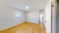 This single-floor residence in St. Louis, MO is laid out in a distinctive long floor plan, offering a practical and efficient use of space across three bedrooms, one bathroom, a kitchen, and a connecting hallway. Light-toned hardwood-style flooring runs throughout the main living areas and bedrooms, contributing to a clean, cohesive aesthetic.

The entry area opens into a bright living space featuring large windows that frame outdoor views and draw in generous natural light. Neutral gray-toned walls and crisp white trim maintain a modern, understated palette throughout. The spacious primary bedroom includes two side-by-side closets with built-in rods and shelving, providing notable storage. Additional bedrooms also feature hardwood-style flooring and windows with outdoor views.

The kitchen is well-appointed with white shaker cabinetry, white subway tile backsplash, gray tile flooring, and a full suite of stainless steel appliances including a dishwasher, range, microwave, and refrigerator. The bathroom features a subway-tiled tub and shower surround, a white vanity, and dark marble-look tile flooring, lending a polished finish. Overall, the unit presents a refreshed, move-in-ready interior with consistent modern detailing.