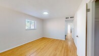 This single-floor residence in St. Louis, MO is laid out in a distinctive long floor plan, offering a practical and efficient use of space across three bedrooms, one bathroom, a kitchen, and a connecting hallway. Light-toned hardwood-style flooring runs throughout the main living areas and bedrooms, contributing to a clean, cohesive aesthetic.

The entry area opens into a bright living space featuring large windows that frame outdoor views and draw in generous natural light. Neutral gray-toned walls and crisp white trim maintain a modern, understated palette throughout. The spacious primary bedroom includes two side-by-side closets with built-in rods and shelving, providing notable storage. Additional bedrooms also feature hardwood-style flooring and windows with outdoor views.

The kitchen is well-appointed with white shaker cabinetry, white subway tile backsplash, gray tile flooring, and a full suite of stainless steel appliances including a dishwasher, range, microwave, and refrigerator. The bathroom features a subway-tiled tub and shower surround, a white vanity, and dark marble-look tile flooring, lending a polished finish. Overall, the unit presents a refreshed, move-in-ready interior with consistent modern detailing.