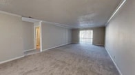 This single-story residence on Horizon Dr W in Jacksonville, Florida offers a practical and well-organized layout across a generously sized floor plan. The living room serves as the central gathering space, featuring plush wall-to-wall carpeting, crown molding, a textured ceiling, and a sliding glass door fitted with vertical blinds that allows natural light to fill the room. The neutral beige tones throughout create a clean, cohesive aesthetic.

The two bedrooms are carpeted and finished with the same neutral palette. The primary bedroom is notably spacious, providing ample room for furnishings, and includes a walk-in closet outfitted with wire shelving for organized storage. The second bedroom is comfortable in scale with a window offering natural light.

Both bathrooms include full tub-and-shower combinations with clean white surrounds. A dedicated laundry closet, accessible via louvered doors, includes washer/dryer hookups and ventilation ducting. Two separate kitchen areas and a connecting hallway contribute to the home's functional versatility. Tile flooring is featured in utility areas, complementing the carpet found throughout the living and sleeping spaces.