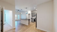 Located at 214 Kingsmeadow Cir in Belville, NC, this thoughtfully designed single-story home offers three bedrooms, two bathrooms, and a comfortable, functional layout. The open-concept kitchen and living area serves as the heart of the home, featuring a large center island with a dark countertop and undermount sink, elegant pendant lighting, and stainless steel appliances including a refrigerator, range, and microwave. Gray shaker-style cabinetry with a classic white subway tile backsplash adds a clean, contemporary aesthetic, while light wood-look flooring flows throughout the main areas. The living space connects seamlessly to the kitchen and provides access to an outdoor area through glass-paneled doors, filling the space with natural light. The bedrooms are carpeted for comfort, each featuring a ceiling fan and bright windows with outdoor views. The spacious primary bedroom includes a dedicated walk-in closet with built-in shelving. Both bathrooms are finished with matching gray vanities, dark countertops, and wood-look flooring — one featuring a tub/shower combo and the other a walk-in shower. A dedicated laundry room houses a full-size washer and dryer, adding everyday convenience to this well-appointed home.