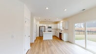 Located in Wake Forest, NC, this well-appointed two-story home offers five bedrooms and three full bathrooms across two spacious floors. The craftsman-style exterior features board-and-batten siding with stone accents, a covered front porch, and an attached two-car garage with a wide concrete driveway. Inside, light wood-tone flooring flows throughout the main living areas, complemented by a neutral, warm color palette that creates a bright and airy atmosphere. The main floor opens into a generous living room and a standout kitchen featuring white shaker cabinets, a central island with pendant lighting, stainless steel appliances, a subway tile backsplash, and a double sink beneath a window. A staircase with wood treads and white balusters connects the floors, leading to the upper level where the spacious primary bedroom includes a large walk-in closet with dual hanging rods. Additional bedrooms are well-sized with natural light from windows overlooking the neighborhood. The bathrooms are cleanly finished with tub-shower combinations and white vanities. A dedicated laundry room and hallways on both floors add to the home's practical layout. The property sits in a newer residential community with sidewalks and landscaped surroundings.
