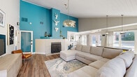Located in Northglenn, CO, this single-floor clubhouse offers a thoughtfully designed open-concept layout that seamlessly connects the living room, dining area, and kitchenette. The space makes an immediate impression with its dramatic vaulted ceilings clad in white shiplap, rich hardwood-style flooring, and a striking bold teal accent wall that anchors the living area. A tile-surround fireplace serves as a central architectural feature, complemented by an elevated display ledge and eclectic white animal-head wall décor that adds personality to the space.

The living area is bright and welcoming, with ample natural light streaming through large windows and glass doors that offer views of the outdoor amenity area. The dining space features vaulted ceilings, pendant lighting, and large windows on multiple walls, creating an airy, sun-filled atmosphere. The compact kitchenette is cleanly appointed with white shaker cabinetry, open shelving, a subway tile backsplash, and dark countertops, providing functional convenience for gatherings. Throughout the space, a cohesive blend of neutral tones, colorful artwork, and modern furnishings creates an inviting and energetic ambiance ideal for community use.