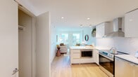 Located on the 8th floor at 100 Harbor Blvd in Hoboken, NJ, this two-bedroom unit offers a well-designed layout with a clean, contemporary aesthetic throughout. Light wood flooring runs continuously across the space, complementing the bright white walls and recessed lighting that give the interior a fresh, airy feel.

The open-concept kitchen flows seamlessly into the living area, making it ideal for everyday living. The kitchen is outfitted with sleek white cabinetry, marble-look stone backsplash and countertops, stainless steel appliances including a range, dishwasher, and a large side-by-side refrigerator, plus a built-in microwave housed in the peninsula. The peninsula also serves as a natural divider between the kitchen and living room.

The living room is bathed in natural light through large windows offering views of the surrounding Hoboken cityscape. A dedicated hallway connects the living areas to the two bedrooms, with a closet conveniently located nearby. The primary bedroom features a window with city views and warm, intimate finishes. The second bedroom is compact yet functional.

The entryway includes a louvered closet door and smart lock, completing this thoughtfully appointed urban residence.