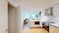 Located on the 8th floor at 100 Harbor Blvd in Hoboken, NJ, this two-bedroom unit offers a well-designed layout with a clean, contemporary aesthetic throughout. Light wood flooring runs continuously across the space, complementing the bright white walls and recessed lighting that give the interior a fresh, airy feel.

The open-concept kitchen flows seamlessly into the living area, making it ideal for everyday living. The kitchen is outfitted with sleek white cabinetry, marble-look stone backsplash and countertops, stainless steel appliances including a range, dishwasher, and a large side-by-side refrigerator, plus a built-in microwave housed in the peninsula. The peninsula also serves as a natural divider between the kitchen and living room.

The living room is bathed in natural light through large windows offering views of the surrounding Hoboken cityscape. A dedicated hallway connects the living areas to the two bedrooms, with a closet conveniently located nearby. The primary bedroom features a window with city views and warm, intimate finishes. The second bedroom is compact yet functional.

The entryway includes a louvered closet door and smart lock, completing this thoughtfully appointed urban residence.