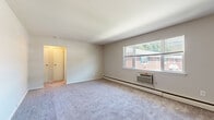Located at 27-55 Green St in Westwood, NJ, this two-bedroom, one-bathroom residence offers a functional single-floor layout designed for comfortable everyday living. The living room is a generously sized space featuring wall-to-wall carpeting, a large multi-pane window that invites ample natural light, a baseboard heating system, and a wall-mounted air conditioning unit for year-round climate control. The kitchen is equipped with a gas range, white tile backsplash, wooden cabinetry, and tile flooring, complemented by a window overlooking greenery outside. The spacious primary bedroom features plush carpeting, a wide window with views of the surrounding brick buildings, and baseboard heating. The second bedroom is well-proportioned with carpet flooring, a window, a closet, and direct access to additional rooms. Both bedrooms offer a clean, neutral aesthetic with white walls and trim. The bathroom is finished with full white tile surrounds, a soaking tub with overhead shower, a single-sink vanity with cabinet storage, and a window for natural ventilation. Throughout the unit, neutral tones and consistent finishes create a cohesive, move-in-ready environment suited for a variety of living arrangements.