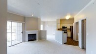 Located at 6805 West Bowles Avenue in Littleton, Colorado, this single-floor residence offers a thoughtfully designed open-concept layout that seamlessly connects the living, dining, and kitchen areas. The living room is anchored by a classic fireplace with a clean white mantle, providing a warm focal point for the space. Plush carpeting throughout the living and dining areas adds comfort underfoot, while durable hardwood-style flooring defines the kitchen zone. A sliding glass door invites natural light and provides convenient access to the outdoors. The kitchen is well-appointed with white cabinetry, stainless steel appliances including a range, microwave, and refrigerator, and a peninsula with bar-height seating that doubles as a casual dining area. A pendant light fixture above the peninsula adds a subtle design touch. The textured ceiling and neutral warm-toned walls create a calm, inviting ambiance throughout. A hallway leads to the additional rooms of the home, offering a practical and efficient floor plan. This residence combines functional design with comfortable finishes, making it a welcoming space in the Littleton community.