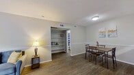 This efficiently designed single-story unit offers a thoughtful layout across a compact footprint. The living room serves as the heart of the space, featuring wood-look flooring, neutral gray walls with a chair rail detail, and a large sliding glass door fitted with vertical blinds that floods the room with natural light. The open flow connects the living area to the dining space, which is accented by built-in shelving that adds both storage and architectural interest.

The galley-style kitchen runs along one wall and includes white cabinetry, a double sink, light stone countertops, and white appliances, offering a clean and functional cooking environment. Wood-look flooring continues throughout the main living areas, creating a cohesive aesthetic.

The bedroom is a comfortable, carpeted retreat equipped with a ceiling fan, a window for natural light, and access to a dedicated walk-in closet featuring dual hanging rods on opposing walls, providing ample storage capacity.

The bathroom includes a wide vanity with a speckled countertop, an undermount sink, white cabinetry, and a large wall mirror with a medicine cabinet above. Neutral tones and textured ceilings throughout the unit contribute to a consistent, understated aesthetic.