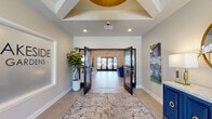 Located at 4406 Helen Rd in Jeffersonville, Indiana, this thoughtfully designed single-story clubhouse offers a polished, contemporary atmosphere across several well-appointed gathering spaces. The entrance foyer sets an immediate tone of sophistication, featuring light wood-look flooring, a statement ceiling detail with a bold gold pendant fixture, teal upholstered benches, and decorative wall sconces that frame glass-paneled entry doors admitting generous natural light.

Beyond the foyer, wide black-framed double doors open into a expansive main gathering area defined by soaring vaulted ceilings with exposed white beams and a striking gold chandelier overhead. A floor-to-ceiling whitewashed brick fireplace anchors one wall, paired with a wall-mounted flat-screen TV, while comfortable seating arrangements of blue sofas and warm accent chairs invite relaxed socializing.

The space flows seamlessly into a game area showcasing a full-size pool table, vibrant abstract artwork, and vaulted ceilings, alongside high-top seating and a fully equipped kitchen with stainless appliances and bar-height seating. Throughout, light wood-look flooring, neutral wall tones, curated artwork, and recessed lighting create a cohesive, inviting ambiance with easy access to outdoor areas through multiple glass doors.
