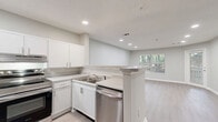 Located at 2423 Martin Luther King Dr in Atlanta, GA, this well-appointed one-bedroom, one-bathroom unit offers a thoughtfully designed single-floor layout. The open-concept kitchen and living area serves as the heart of the home, featuring light wood-look luxury vinyl flooring, neutral gray walls, and recessed lighting throughout. The kitchen is outfitted with white shaker-style cabinetry, light stone countertops, a peninsula with additional counter space, and a full suite of stainless steel appliances including a range, dishwasher, and refrigerator. The living area is bright and airy, benefiting from multiple windows that invite natural light and offer views of surrounding greenery, along with a private exterior door. The bedroom is carpeted for comfort and includes a window with outdoor views, providing a quiet retreat. A dedicated closet offers organized storage. The full bathroom features a tiled tub/shower combo equipped with accessibility grab bars and brushed nickel fixtures. A separate laundry area with washer/dryer hookups and overhead shelving adds everyday convenience. Clean finishes and a cohesive neutral palette give the entire unit a fresh, modern feel.