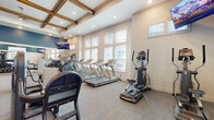 Located at 464 S Kirkman Rd in Orlando, Florida, this well-appointed fitness center offers a comprehensive workout facility spread across a single floor. The space is characterized by soaring ceilings with decorative exposed wood beams, recessed lighting, and an abundance of natural light streaming through large windows dressed with white blinds. The walls feature a striking two-tone design, with deep navy blue accents contrasting against crisp white wainscoting.

The cardio zone is generously equipped with multiple treadmills, elliptical trainers, a stair climber, stationary bikes, and a rowing machine, with wall-mounted flat-screen TVs positioned throughout for entertainment during workouts. The strength training area houses a cable machine, a Smith machine, a full dumbbell rack, and a weight bench, all reflected in floor-to-ceiling mirrors that enhance the sense of space.

A dedicated open studio area provides ample room for functional training and features a plyometric box and spin bike, with large windows offering views of the outdoor surroundings including palm trees. A convenient Hydration Station serves as a central amenity hub, complete with a beverage cooler and towel storage. Neutral carpet flooring throughout ties the space together, creating a clean, modern, and motivating environment for residents.