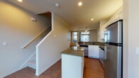 Located at 2083 SW River Dr in Portland, Oregon, this multi-level apartment spans three floors and offers a well-designed layout with a variety of functional spaces. The entry-level garage provides private parking and includes an in-unit washer and dryer area with overhead shelving, offering convenient laundry access alongside a water heater and utility connections.

The main living level features warm hardwood-style flooring throughout, an open-concept kitchen and living area, and a ceiling fan overhead. The kitchen is equipped with stainless steel appliances, including a refrigerator, range, and dishwasher, complemented by granite countertops, a central island, and white cabinetry. Recessed lighting and a large window brighten the space. Sliding glass doors open to a private balcony, bringing in natural light and outdoor access.

The upper floor includes a carpeted bedroom with a generous closet and a window overlooking the surrounding neighborhood. A full bathroom on this level features a tub-shower combo with tile surround, a single vanity, and hardwood-style flooring. A second bathroom offers a separate shower stall, toilet, and vanity. The staircase connecting all three levels is cleanly finished with white railings, reinforcing the cohesive and tidy aesthetic found throughout this well-appointed Portland residence.