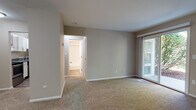 The Medium is a thoughtfully designed 1-bedroom, 1-bathroom residence that offers a comfortable and functional single-floor layout. The living area is generously sized, featuring soft wall-to-wall carpeting, neutral taupe-toned walls, and a sliding glass door that opens to a private balcony, allowing natural light to fill the space and providing pleasant outdoor views. A separate entryway with direct access leads seamlessly into the living area, which connects to the kitchen. The kitchen is a standout feature, showcasing white shaker-style cabinetry, granite countertops, wood-look vinyl flooring, and a full suite of stainless steel appliances including a refrigerator and dishwasher. The bedroom is a well-proportioned retreat with plush carpeting, neutral walls, and a built-in closet equipped with multiple shelving units for ample storage. The full bathroom is finished with consistent granite countertops on the white vanity, a mirrored cabinet, wood-look vinyl flooring, and a tub-shower combination with clean white tile surround. Throughout the residence, the design maintains a cohesive, neutral palette that creates a calm and move-in-ready atmosphere suited for everyday living.
