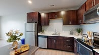 Located at 2141 S Robinson Ave in Milwaukee, Wisconsin, this 1-bedroom, 1-bathroom unit offers a thoughtfully designed single-level layout that maximizes functionality and comfort. The open-concept kitchen and living area forms the heart of the space, featuring rich dark-walnut cabinetry extending to the ceiling for ample storage, light-toned countertops, a stainless steel appliance suite including a refrigerator, dishwasher, and range with microwave, and durable wood-look flooring that runs throughout. Recessed lighting illuminates the kitchen, adding a polished, modern feel. The bedroom is a comfortable, well-proportioned retreat finished with soft carpeting and a large window that invites natural light and outdoor views. A dedicated closet with built-in shelving provides organized storage. The bathroom is clean and contemporary, showcasing a dark wood vanity with an undermount sink, a large wall mirror, light tile flooring, and a full tub-shower combination. Neutral gray tones throughout the unit create a cohesive, calm aesthetic. The overall design balances practicality with modern style, making this an efficient and inviting living space.