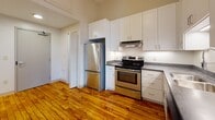 Located at 95 Chestnut St in the heart of Providence, Rhode Island, this loft-style unit blends industrial character with modern updates throughout. Rich, warm-toned hardwood floors run continuously across the open layout, complementing the exposed brick walls and large black-framed industrial windows that flood the space with abundant natural light and frame views of the surrounding urban streetscape.

The kitchen is well-appointed with crisp white shaker cabinetry extending to the ceiling for generous storage, dark stone countertops, stainless steel appliances including a refrigerator and electric range, an under-cabinet range hood, and a double-basin stainless steel sink — a functional and attractive space for cooking and entertaining.

The bedroom area offers a dedicated closet with built-in rod and shelving, providing practical storage. A stacked washer and dryer unit is conveniently accessible nearby, adding everyday ease to the layout. The full bathroom features clean white tile flooring, a vanity with under-sink cabinetry, a wall-mounted mirror, and modern fixtures throughout. A programmable thermostat is positioned in the hallway for easy climate control. The overall ambiance is one of urban loft living, with the character of a converted industrial building harmoniously balanced by contemporary finishes.