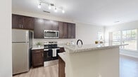 This single-story, one-bedroom, one-bathroom residence offers a thoughtfully designed layout that maximizes functionality and comfort. The kitchen serves as a standout feature, showcasing rich dark-espresso shaker-style cabinetry extending to the ceiling, light granite countertops, and a full suite of stainless steel appliances including a refrigerator, electric range, and over-the-range microwave. A peninsula with matching granite provides additional prep space and connects the kitchen to the dining area, creating an open, cohesive flow. Light wood-look flooring runs throughout the main living areas, complementing the neutral wall tones and giving the space a clean, contemporary feel. The bedroom is a comfortable retreat with plush carpeting, dual windows that invite natural light and outdoor views, and direct access to a dedicated walk-in closet outfitted with wire shelving for organized storage. The bathroom is finished with the same dark cabinetry seen in the kitchen, granite countertops, a full tub-shower combination, and light wood-look flooring, maintaining a consistent design language throughout. Crown molding accents add a refined architectural touch to the living areas, rounding out this well-appointed residence.