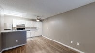 This single-floor unit offers a practical and functional layout across several well-defined living areas. The open kitchen serves as a central hub, featuring crisp white cabinetry, speckled light countertops, and stainless steel appliances including an electric range and refrigerator. A peninsula provides additional prep space and separates the kitchen from the adjacent living area. Light wood-look vinyl flooring flows throughout the main living spaces, complemented by neutral gray-toned walls and white baseboards that create a clean, cohesive aesthetic. A ceiling fan overhead adds comfort to the living area, which benefits from natural light through blinds-fitted windows. The textured popcorn ceilings are consistent throughout the unit. The bedrooms are carpeted and generously proportioned, each featuring windows that allow in natural light and ample wall space for furniture placement. The bathroom is efficiently designed, offering a full tub and shower combination with a white surround, a single-sink vanity with storage cabinetry below, and a wall mirror. The entry area provides a welcoming transition into the living space, also finished with wood-look flooring and a window for added light. Overall, the unit presents a neutral, move-in-ready interior with consistent finishes throughout.