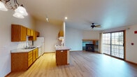 This single-floor residence offers a thoughtfully designed open-concept layout that seamlessly connects the kitchen, dining, and living areas. The kitchen is outfitted with warm honey-toned oak cabinetry, light granite-style countertops, a breakfast bar peninsula, and white appliances including a range, dishwasher, and refrigerator. Track lighting and recessed fixtures illuminate the workspace efficiently. The kitchen flows naturally into the dining area, which features a pendant chandelier, and onward into the spacious living room. The living room is anchored by a built-in gas fireplace with a tile surround, a ceiling fan, and a sliding glass door that opens to a private balcony, filling the space with natural light. The bedrooms are carpeted with neutral tones, feature wood-trimmed windows with blinds, and include closets with wood-paneled sliding doors. The primary bathroom includes a wide oak vanity, a large mirror with a lighted bar, and a step-in shower. A second bathroom serves the remaining bedrooms and conveniently adjoins an in-unit laundry room equipped with a stacked washer and dryer. Light hardwood-style flooring flows throughout the main living areas, complemented by warm oak trim throughout, creating a cohesive and inviting aesthetic across the entire residence.