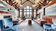 Located in Thornton, Colorado, this single-story community clubhouse at 12150 Washington Center Pkwy is an architecturally striking gathering space defined by its dramatic vaulted ceiling with exposed dark-stained timber trusses and oversized pendant lighting. The grand main lounge serves as the heart of the facility, anchored by a floor-to-ceiling stacked stone fireplace with a rich wood mantle. Expansive multi-pane windows flood the space with natural light and offer direct views of the outdoor pool area, while leather sofas and upholstered wingback chairs create an inviting, resort-like atmosphere. Slate tile flooring in the entry transitions seamlessly into patterned carpet throughout the lounge. A formal entry foyer welcomes visitors with a coffered ceiling, decorative pendant, and rich wood wainscoting. The game and media lounge features a wall-to-wall custom cherry wood built-in entertainment center, comfortable seating, a billiards table, and a dedicated workspace. A well-appointed catering kitchen includes rich cherry cabinetry, polished granite countertops, stainless steel appliances, an island bar with seating, and a full sink — ideal for hosting events. Together, these spaces offer a sophisticated and functional environment for community gatherings.