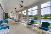 Located at 8400 Veterans Pkwy in Columbus, Georgia, this expansive covered porch serves as a welcoming transitional space between interior facilities and outdoor amenities. The elongated, single-floor structure is defined by its bright, airy design, with floor-to-ceiling windows and glass-paneled walls running the length of the space, flooding the interior with abundant natural light and offering unobstructed views of the surrounding pool area and lush greenery beyond.

The flooring features a classic herringbone-patterned brick, adding texture and visual interest underfoot. Overhead, a white beadboard ceiling fitted with multiple modern ceiling fans ensures comfortable airflow throughout the space. Bold, vibrant accents energize the design — most notably the striking orange and red-framed doors that punctuate the gray-sided interior wall, creating eye-catching focal points along the corridor.

Furnishings are arranged thoughtfully throughout, including white lattice-frame lounge sofas and chairs cushioned in vivid teal, alongside glass-top accent tables that invite casual gatherings. A hanging porch swing adds a leisurely touch, while large potted tropical plants contribute to the relaxed, resort-like atmosphere. Bold red French doors open directly to the pool deck, seamlessly connecting indoor comfort with outdoor recreation. The overall ambiance is lively, welcoming, and well-suited for communal relaxation.