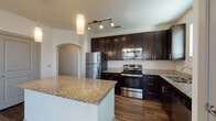 This single-floor residence showcases a cohesive, modern design throughout its well-organized layout. The kitchen serves as a central highlight, featuring rich dark cabinetry that extends to the ceiling for ample storage, complemented by granite countertops and a full suite of stainless steel appliances, including a refrigerator, range, microwave, and dishwasher. A substantial kitchen island provides additional prep and dining space, while pendant and track lighting add a polished, functional ambiance. Wood-look flooring flows through the kitchen and connects seamlessly to adjoining areas via an arched passageway, adding an architectural touch.

The bathrooms mirror the kitchen's refined aesthetic, featuring dark vanity cabinetry topped with matching granite, tile-surround tub and shower combinations, and wood-look flooring. One bathroom includes direct access to a spacious walk-in closet with built-in shelving and hanging rods.

Bedrooms are finished with plush carpet, generous natural light from large windows with blinds, and ceiling fans for added comfort. Hallways are neatly designed with neutral textured walls and carpeted flooring, contributing to the unit's clean, contemporary feel throughout.