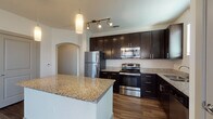 This single-floor residence showcases a cohesive, modern design throughout its well-organized layout. The kitchen serves as a central highlight, featuring rich dark cabinetry that extends to the ceiling for ample storage, complemented by granite countertops and a full suite of stainless steel appliances, including a refrigerator, range, microwave, and dishwasher. A substantial kitchen island provides additional prep and dining space, while pendant and track lighting add a polished, functional ambiance. Wood-look flooring flows through the kitchen and connects seamlessly to adjoining areas via an arched passageway, adding an architectural touch.

The bathrooms mirror the kitchen's refined aesthetic, featuring dark vanity cabinetry topped with matching granite, tile-surround tub and shower combinations, and wood-look flooring. One bathroom includes direct access to a spacious walk-in closet with built-in shelving and hanging rods.

Bedrooms are finished with plush carpet, generous natural light from large windows with blinds, and ceiling fans for added comfort. Hallways are neatly designed with neutral textured walls and carpeted flooring, contributing to the unit's clean, contemporary feel throughout.