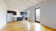 Located on the 8th floor at 215 W Pershing Rd in Kansas City, Missouri, this one-bedroom, one-bathroom unit showcases a compelling blend of industrial character and modern finishes. The open living area greets you with warm hardwood floors, bright white walls, and striking exposed beam ceilings fitted with track lighting — a nod to the building's architectural heritage. The kitchen flows seamlessly from the living space and features dark espresso cabinetry, a white subway tile backsplash, stainless steel appliances including a range, dishwasher, and refrigerator, and ample counter space for everyday cooking. A hallway connects the main living area to the private bedroom, which is finished with plush carpet, exposed beam ceilings with a ceiling fan, and a window offering outdoor views of greenery. The bedroom also includes a closet and an in-unit stacked washer and dryer, adding everyday convenience. The bathroom is clean and contemporary, featuring white tile walls, a glass-enclosed shower-tub combination, a dark vanity with brushed nickel hardware, and large-format tile flooring. Throughout the unit, consistent use of neutral tones and quality finishes creates a cohesive, functional living environment.