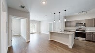 This single-story unit in Little Rock, Arkansas, presents a clean, contemporary design with a neutral color palette and wood-style flooring carried consistently throughout the space. The open-concept living and kitchen area serves as the central hub of the floor plan, where a granite-topped island anchors the kitchen and provides additional workspace and seating. Three pendant lights hang above the island, adding a modern touch while illuminating the space. The kitchen is well-equipped with gray shaker-style cabinetry, granite countertops, and a full suite of stainless steel appliances, including a range, microwave, and refrigerator. The adjoining living area benefits from natural light provided by French doors, creating a bright and welcoming atmosphere.

The bedrooms are generously proportioned, each featuring ceiling fans and ample closet space. One bedroom includes a walk-in closet with direct access to a bathroom. The bathrooms are finished with granite-topped vanities, dark cabinetry with brushed nickel hardware, large mirrors, and wood-style flooring. One bathroom includes a tub-shower combination, while another features a separate shower. Throughout the unit, white trim and neutral walls contribute to a cohesive, move-in-ready aesthetic.