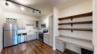 Located at 321 S Swing Rd in Greensboro, NC, this single-story unit offers a thoughtfully designed layout with modern finishes throughout. Rich hardwood-style flooring extends across the main living areas, anchoring an open-concept space that connects the living area to the kitchen seamlessly. Track lighting illuminates the space, highlighting the clean, contemporary aesthetic.

The kitchen is a standout feature, equipped with gray shaker-style cabinetry, granite countertops, a classic white farmhouse sink, and a white subway tile backsplash. Stainless steel appliances — including a refrigerator, electric range, microwave, and dishwasher — complement the design. Built-in open wood shelving and a dedicated desk area provide additional functionality.

The bedrooms are carpeted for comfort, each offering generous walk-in closets outfitted with wire shelving systems for organized storage. A ceiling fan adds convenience to the primary bedroom, which also benefits from natural light through large windows.

Two bathrooms serve the unit — one featuring a tiled walk-in shower with built-in niches and granite vanity, and another with a full soaking tub and shower combination, overhead cabinetry, and matching granite countertops. The consistent use of gray cabinetry and granite surfaces ties the entire space together cohesively.