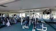 Located at 303 W State Street in the heart of Doylestown, PA, this fitness facility offers a well-appointed, single-floor gym designed to support a comprehensive workout experience. The open exercise floor is outfitted with an extensive selection of equipment, including TuffStuff multi-station cable machines, free weight benches, dumbbell racks, and a variety of cardiovascular machines such as ellipticals and steppers. Full-length mirrors line the walls, amplifying the sense of space and allowing users to monitor their form throughout their workouts. Large windows along the perimeter flood the space with natural light and provide views of the surrounding greenery, creating an energizing and pleasant environment. The low ceiling features exposed ductwork, contributing to a functional, utilitarian aesthetic. Dark carpeted flooring throughout the workout area provides both comfort underfoot and a practical surface for equipment placement. The layout is thoughtfully organized to maximize usable floor space, accommodating a diverse range of training styles from strength training to cardio conditioning, making it a versatile and well-equipped destination for fitness enthusiasts.