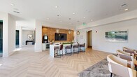 Located at 4271 Woodward Mill Rd in Buford, Georgia, this single-story community clubhouse showcases a sophisticated and thoughtfully designed interior. The space is unified by striking light-toned herringbone wood flooring that flows seamlessly throughout, lending a sense of refined elegance to every area.

The main gathering area centers around a sleek white island with leather bar seating, set against a warm textured tile accent wall that frames a large flat-screen television. Globe pendant lights hang overhead, while built-in cabinetry and a coffee station provide functional amenities for residents and guests.

A separate lounge area offers a more intimate setting, featuring a cushioned bench sofa, round accent tables, and upholstered chairs arranged beneath a trio of decorative wall panels illuminated by gold-toned wall sconces. This space is ideal for casual conversation or relaxed gatherings.

A glass-walled conference room provides a professional setting equipped with a large meeting table, ergonomic seating, and a mounted display screen — perfect for private meetings or business use. Elegant arched doorways connect the various zones, adding an architectural flourish throughout.

The sun-filled entry foyer welcomes visitors with large windows, sheer drapery, and curated décor, establishing a bright and inviting first impression for the entire facility.