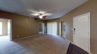 This single-story residence offers a practical and comfortable layout designed to maximize usable space. The living room serves as the central hub of the home, featuring warm beige carpeting, a textured ceiling, and a ceiling fan with integrated lighting. A large sliding glass door fitted with vertical blinds admits generous natural light, while a built-in bookshelf and a dedicated entry area with a front door add functional detail to the space. The living room also connects openly to the dining area via a pass-through window, enhancing the sense of connectivity between rooms.

The galley-style kitchen is efficiently designed with white cabinetry lining both sides, granite-style countertops, and black appliances including a range, refrigerator, microwave, and dishwasher. Dark wood-style flooring runs throughout the kitchen, providing a clean contrast to the light cabinetry.

The bedroom is a generously sized, carpeted room with warm neutral walls and its own ceiling fan. The bathroom features dark hardwood-style flooring, white cabinetry, granite-style countertops, dual vanity mirrors with overhead lighting, and ample storage, offering a clean and functional design throughout.