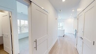 Located at 5945 Arlo Dr in Indianapolis, Indiana, this one-bedroom, one-bathroom residence offers a clean, modern aesthetic defined by bright white walls, light wood-tone flooring, and an abundance of natural light. The open-concept kitchen and dining area serves as the heart of the home, anchored by a large center island with a white quartz countertop and undermount sink. White shaker-style cabinetry lines the walls, complemented by stainless steel appliances including a range, microwave, refrigerator, and dishwasher. Recessed lighting and large sliding glass doors enhance the airy feel of this space. A stylish sliding barn door adds a contemporary architectural touch, leading into the hallway connecting the remaining rooms. The bedroom is a comfortable, well-proportioned space featuring plush carpeting and a sizable window with blinds that frame views of the surrounding greenery. The full bathroom is finished with light beige tile in the tub-shower surround, wood-tone flooring, and white cabinetry. A dedicated closet provides practical storage. Throughout the unit, the consistent use of neutral tones and modern finishes creates a cohesive, move-in-ready living environment.