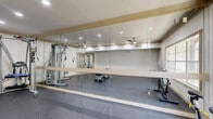 Located at 2727 Elmside Dr in Houston, TX, this dedicated exercise room offers a well-appointed fitness space designed for effective full-body training. The room features durable speckled rubber flooring throughout, providing cushioning and traction ideal for a variety of workout activities. Crown molding and recessed lighting lend a polished, refined aesthetic to the space, while a ceiling fan ensures comfortable air circulation during workouts.

A large wall of floor-to-ceiling mirrors spans one side of the room, enhancing the sense of openness and allowing users to monitor their form during exercise. The room is equipped with a Hoist multi-station cable machine, an adjustable weight bench, and a spin bike, offering a comprehensive range of strength and cardio training options. Natural light filters in through large windows, creating a bright and energizing environment.

Access to the room is provided through a set of glass-panel French doors, seamlessly connecting it to the rest of the property. An additional interior door with louvered panels provides further convenience. The clean white walls, elegant crown molding, and thoughtful layout combine to create a functional yet visually appealing fitness space suited for dedicated exercise routines.