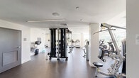 Located at 10 Patriot Pkwy in Weymouth, MA, this fitness center is a generously sized, single-floor exercise facility designed to support a full spectrum of workout routines. The space features a clean, modern aesthetic with white walls, recessed lighting, and dark rubberized flooring throughout, creating a professional and functional environment.

The cardio zone is prominently featured along one side of the main floor, lined with a row of Cybex treadmills, elliptical machines, and upright stationary bikes, several of which are equipped with personal display screens. Large windows throughout this area flood the space with natural light and provide views of the surrounding greenery, enhancing the workout experience.

The strength training area is equally well-appointed, featuring a multi-station cable and functional trainer rig, a full rack of dumbbells, weight benches, and a selection of selectorized resistance machines targeting various muscle groups. A dedicated functional training room provides additional space for dynamic exercises, equipped with medicine balls, stability balls, resistance bands, balance tools, a rowing machine, and a large wall mirror with a wooden bench — ideal for stretching and accessory work.

Full-length mirrors are strategically placed throughout the facility to support proper form and add to the sense of openness. The overall layout is thoughtfully organized to accommodate simultaneous use across multiple training disciplines.