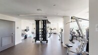 Located at 10 Patriot Pkwy in Weymouth, MA, this fitness center is a generously sized, single-floor exercise facility designed to support a full spectrum of workout routines. The space features a clean, modern aesthetic with white walls, recessed lighting, and dark rubberized flooring throughout, creating a professional and functional environment.

The cardio zone is prominently featured along one side of the main floor, lined with a row of Cybex treadmills, elliptical machines, and upright stationary bikes, several of which are equipped with personal display screens. Large windows throughout this area flood the space with natural light and provide views of the surrounding greenery, enhancing the workout experience.

The strength training area is equally well-appointed, featuring a multi-station cable and functional trainer rig, a full rack of dumbbells, weight benches, and a selection of selectorized resistance machines targeting various muscle groups. A dedicated functional training room provides additional space for dynamic exercises, equipped with medicine balls, stability balls, resistance bands, balance tools, a rowing machine, and a large wall mirror with a wooden bench — ideal for stretching and accessory work.

Full-length mirrors are strategically placed throughout the facility to support proper form and add to the sense of openness. The overall layout is thoughtfully organized to accommodate simultaneous use across multiple training disciplines.
