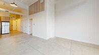 Located at 450 Amsterdam St in Detroit's vibrant New Center neighborhood, this 2-bedroom, 2-bathroom loft-style unit showcases an impressive blend of industrial character and modern design. Polished concrete floors run throughout the entire space, complementing the soaring ceilings that lend an open, airy feel well beyond what the floor plan might suggest. The living area is anchored by dramatic floor-to-ceiling industrial windows and exposed brick walls, allowing natural light to pour in and highlighting the building's rich architectural heritage. A hallway leads seamlessly from the entry through the space, lined with clean white walls and pendant lighting overhead. The contemporary kitchen features light wood cabinetry, stainless steel appliances including a refrigerator, electric range, microwave, and dishwasher, paired with white countertops for a crisp, functional aesthetic. Both bedrooms offer clean, minimalist interiors with high ceilings and ample wall space; the primary bedroom includes a sliding closet door. The two bathrooms are thoughtfully finished — one with a full soaking tub and floor-to-ceiling subway tile surround, and the other with a walk-in tiled shower and warm wood vanity. A dedicated laundry room and closet round out this well-appointed urban retreat.