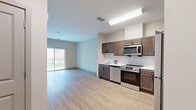 This single-floor, 3-bedroom, 2-bathroom residence at Fort George G. Meade, MD offers a practical and modern layout designed for comfortable living. The open-concept kitchen and living area forms the heart of the home, featuring rich dark brown cabinetry, a classic white subway tile backsplash, and a full suite of stainless steel appliances including a range, over-the-range microwave, dishwasher, and refrigerator. Light wood-style flooring runs throughout the main living areas, creating a clean and cohesive look.

The living area is bright and open, with a sliding glass door that leads to a private balcony overlooking a lush, tree-lined outdoor setting, filling the space with natural light. The bedrooms are carpeted for comfort, with the primary bedroom offering generous proportions and windows with views of the surrounding greenery. A dedicated closet provides convenient storage adjacent to one of the bedrooms.

The two bathrooms are finished with neutral tile flooring and clean white tile surrounds. One bathroom features a tub-shower combination with a glass panel, while the other offers a walk-in glass-enclosed shower. The overall aesthetic is contemporary and understated, with neutral tones throughout that create a calm and functional living environment.
