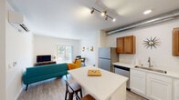 This well-appointed single-floor unit offers a thoughtfully designed open-concept layout that seamlessly connects the kitchen, dining, and living areas. The kitchen is equipped with stainless steel appliances, warm-toned wood upper cabinetry, crisp white lower cabinets, and a quartz-topped island with bar seating — ideal for casual dining or meal prep. An exposed metal ductwork detail adds an industrial-modern accent to the space. The living area is bright and welcoming, anchored by large sliding glass doors that open to a private balcony overlooking lush greenery, filling the room with natural light. A dedicated in-unit stacked washer and dryer adds everyday convenience. The two bedrooms are comfortably sized with plush carpeted floors, large windows, and generous closet space — one featuring a walk-in closet with direct access to the bathroom. The bathroom is clean and functional, featuring a white vanity with an undermount sink, a framed mirror, and wood-look flooring that ties the space together. Throughout the unit, light wood-look flooring in the main living areas and a neutral white palette create a bright, cohesive, and modern atmosphere.