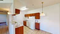 This single-floor unit offers a practical and well-organized layout across two bedrooms and two bathrooms. The kitchen is efficiently designed in a galley-style configuration, featuring warm medium-toned wood cabinetry that lines both walls, providing ample storage. White appliances, including a refrigerator, electric range with overhead microwave, and dishwasher, are neatly integrated throughout. Light ceramic tile flooring extends through the kitchen and into the adjoining dining area, which is illuminated by a brass pendant light. The combined kitchen and dining space opens to a larger tiled living area, creating a connected and functional common zone.

The primary bedroom features plush carpet flooring, a ceiling fan with light fixture, and a sliding glass door offering direct outdoor access and natural light. A dedicated walk-in closet equipped with multiple hanging rods and shelving provides generous storage. The second bedroom is carpeted and receives natural light through a window with exterior views. Both bathrooms are finished with tile flooring and include a full tub-shower combination, toilet, and vanity with sink. The overall aesthetic is clean and neutral throughout.