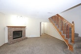 This two-floor home offers a well-organized layout with functional living spaces throughout. The main level features an open living and dining area with plush carpeting, a ceiling fan, and a striking brick fireplace accented by track lighting — a natural focal point for the room. The kitchen is efficiently designed with warm oak cabinetry, a full suite of black appliances including a refrigerator, electric range, and dishwasher, complemented by tile-style flooring and a window above the sink. A carpeted staircase with a classic wood railing connects the levels. The upper floor hosts multiple bedrooms, each carpeted and featuring ceiling fans and natural light from windows with blinds. The primary bedroom boasts vaulted ceilings and a walk-in closet with mirrored sliding doors. Additional bedrooms include standard closets. The bathrooms are finished with oak-framed vanities, tile-style flooring, and a full tub/shower combination. A half bath on one level features a clean, simple vanity with a large mirror. Warm neutral tones and consistent oak wood trim details carry throughout the home, creating a cohesive and practical living environment across both floors.