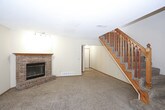 This two-floor home offers a well-organized layout with functional living spaces throughout. The main level features an open living and dining area with plush carpeting, a ceiling fan, and a striking brick fireplace accented by track lighting — a natural focal point for the room. The kitchen is efficiently designed with warm oak cabinetry, a full suite of black appliances including a refrigerator, electric range, and dishwasher, complemented by tile-style flooring and a window above the sink. A carpeted staircase with a classic wood railing connects the levels. The upper floor hosts multiple bedrooms, each carpeted and featuring ceiling fans and natural light from windows with blinds. The primary bedroom boasts vaulted ceilings and a walk-in closet with mirrored sliding doors. Additional bedrooms include standard closets. The bathrooms are finished with oak-framed vanities, tile-style flooring, and a full tub/shower combination. A half bath on one level features a clean, simple vanity with a large mirror. Warm neutral tones and consistent oak wood trim details carry throughout the home, creating a cohesive and practical living environment across both floors.